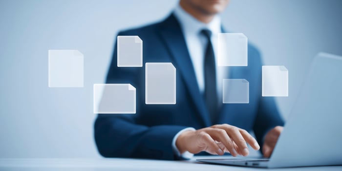 Businessman in formal attire working on laptop with floating document icons representing digital file management and organization in modern workspace photo