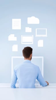 Man in blue shirt working at a computer with digital icons representing files and documents floating above in a modern workspace with copy space photo