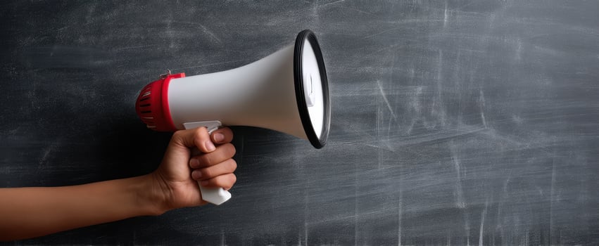 The megaphone held in hand against a blank chalkboard background. photo