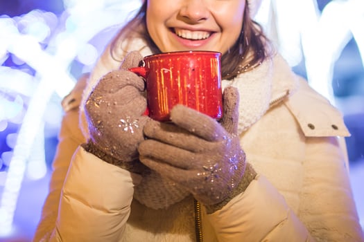 Woman standing over winter christmas city background snow snow drifts, stands warm jacket hat, holds cup tea with hot tea drinks photo