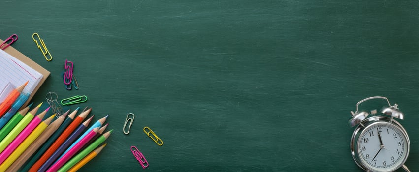 The colorful pencils and alarm clock on a green chalkboard background. photo