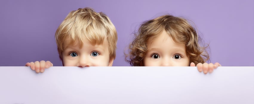 The curious children peeking over a pastel backdrop with bright expressions. photo