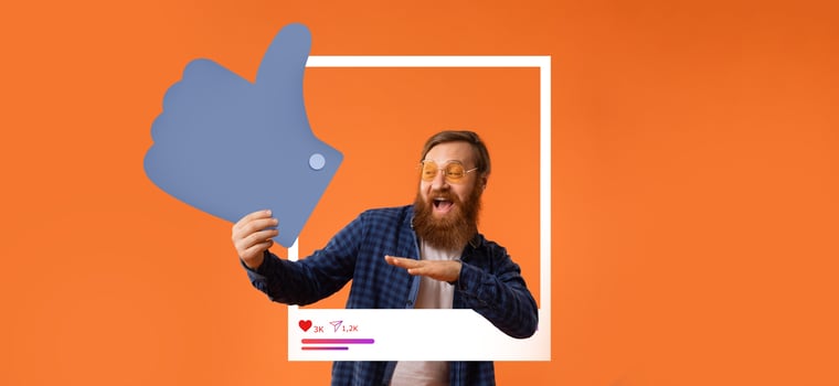 A man with a beard and glasses celebrates his success by making a thumbs up gesture while engaging with his online audience. The bright orange background enhances his joyful expression. photo