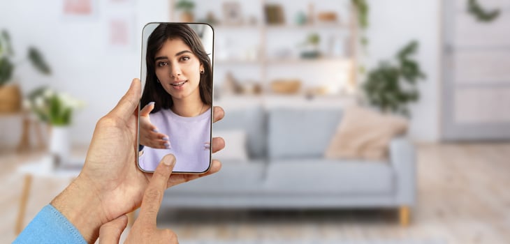 A person connects with someone through a smartphone during a call. The setting is a cozy home with a light-filled living room. The interaction appears warm and engaging. photo