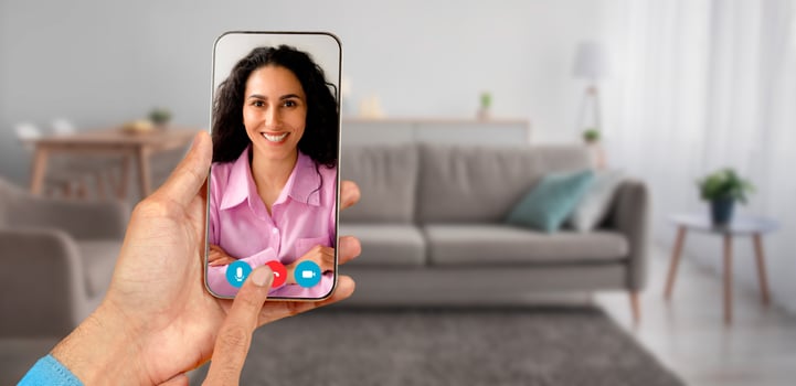 A person participates in a call using a smartphone, interacting with smiling woman from a cozy home environment. The setting includes a modern living room with comfortable furniture. photo