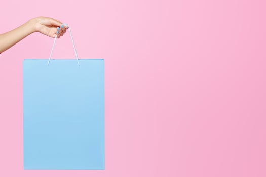 Great sale offer and ad space. Hand of teen african american woman holding blue shopping bag with purchase with blank space isolated on pink background, vertical, cropped, studio shot, close up photo