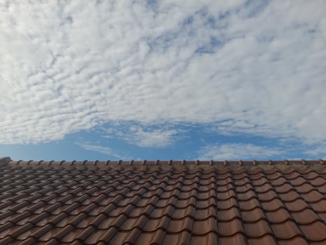 A tiled rooftop under a sky filled with scattered clouds and patches of blue. The scene captures a peaceful, sunny day with a blend of architectural and natural elements. photo