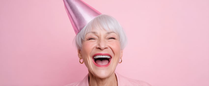 The joyful elderly woman with a pink party hat celebrating life with a big smile. photo