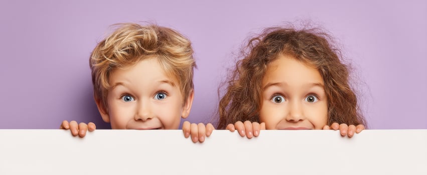 The cheerful children hiding behind a blank banner with playful expressions. photo
