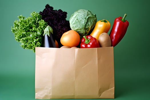 Fresh assorted vegetables are overflowing from a brown paper bag on green backdrop photo