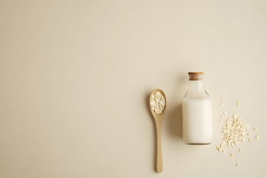 Fresh oat milk in a glass bottle sits beside a wooden spoon with oats photo