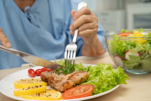 senior woman eating pork chop stake and vegetable salad for healthy food in hospital. photo