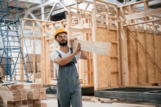 Walking, holding plank. Industrial worker in wooden warehouse photo