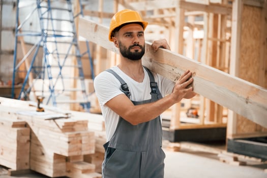 Front view, holding plank. Industrial worker in wooden warehouse. photo