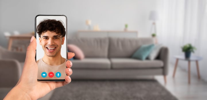 A person holding a smartphone during a call at home. The cozy living room features a sofa and soft lighting, creating a comfortable atmosphere for virtual interaction. photo