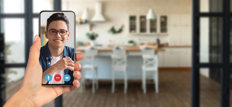A person is engaged in an online call using a smartphone in a stylish home kitchen. The setting features a bright, open space with modern furniture and decor, creating a warm ambiance. photo