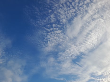 A serene sky filled with soft, scattered white clouds under a bright blue backdrop, evoking calm and peaceful vibes. photo