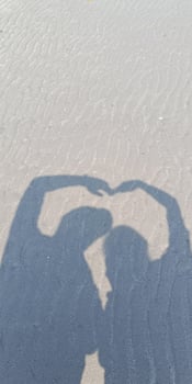 Silhouette of a couple forming heart shape with their hands on sandy beach. Sweet moments together photo