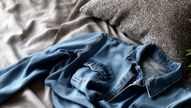 Faded denim shirt on a bed with gray linens and pillow photo