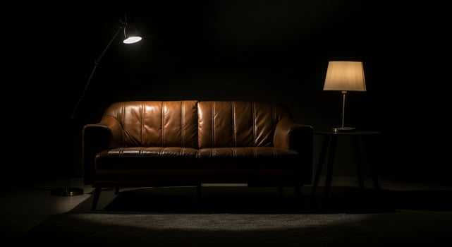 Elegant brown leather sofa illuminated by soft light from a nearby lamp, creating a cozy atmosphere in a darkened room with minimalistic decor and inviting ambiance photo