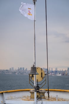 Bosphorus view from a boat with flag flying and bell in foreground on a calm and cloudy day photo