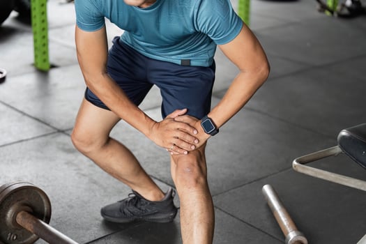 Fitness Injury Prevention. Man holding knee in gym after workout. photo