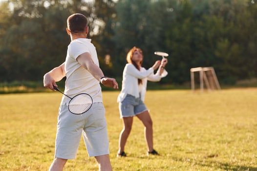 Weekend, activities. Man with woman are playing badminton on the field photo