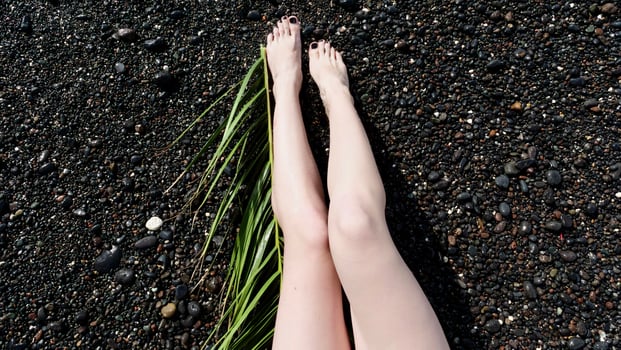 A woman's legs are on a black beach with grass photo