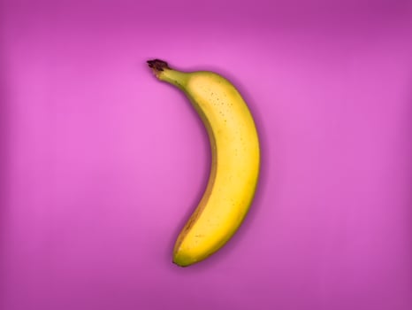 One bright yellow banana, lying vertically on a purple background, top view, center of image turned left photo