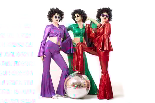 Three female pop stars in neon clothes pose in front of a silver ball photo