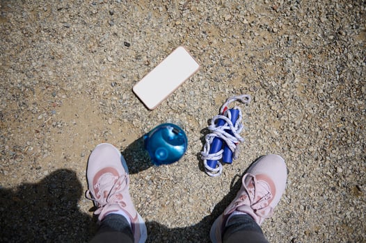 Pink Sneakers on Gravel Surface with Fitness Items Including Water Bottle, Smartphone, and Jump Rope photo