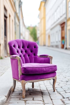 Vintage purple velvet armchair with tufted backrest and ornate wooden frame is placed on a cobblestone street, showcasing elegance and charm in an urban setting photo