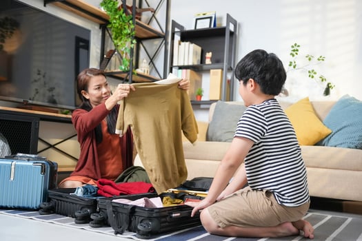 Happy Asian Family Getting Ready for Travel at Home, Folding Clothes into Suitcases, Family Preparing for Trip, Mother and Son Packing Luggage Together for Vacation photo