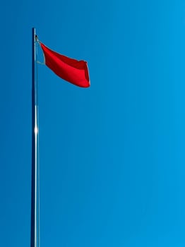 A red flag flutters in the wind in the blue sky by the sea during the day. photo