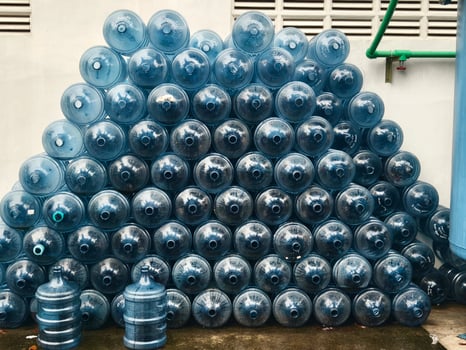Large Stack of Blue Plastic Reusable Water Cooler Gallons Arranged in a Pyramid Formation Outdoors photo