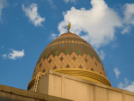 Ornate Mosque Dome with Crescent Moon Symbol Against Blue Sky and White Clouds photo