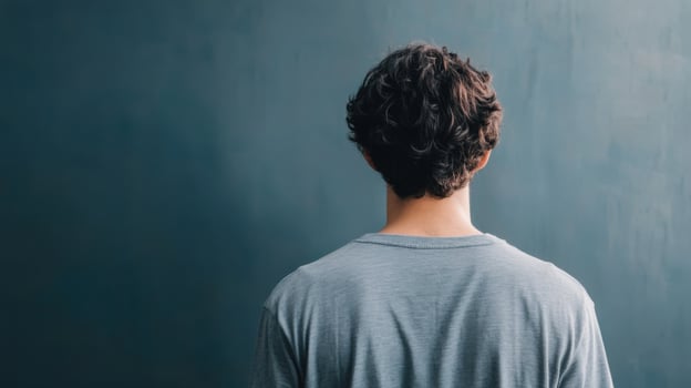 Contemplative Pose A Rear View of a Man with Curly Hair, Dressed in a Grey Shirt Against a Blue Wall. The image exudes a sense of calm and introspection. photo