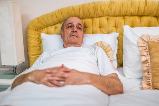 Senior man lying in bed, appearing sad and anxious, struggling with insomnia and loneliness in the early morning light. photo