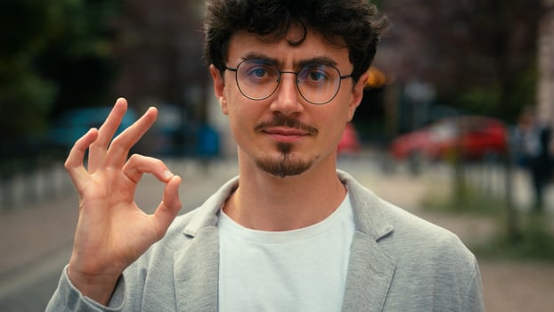 Close up portrait Hispanic business man male guy showing ok gesture in city male guy in glasses show okay sign fine good result excellent reaction outdoors at street businessman recommend joyful glad photo