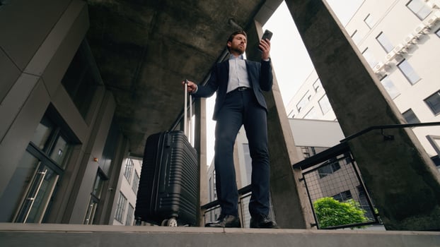 Confused business man holding mobile phone in city with suitcase baggage arrive puzzled looking around waiting taxi lost in new town Caucasian businessman middle-aged male luggage arriving problem photo