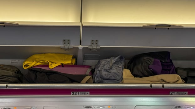 Overflowing airplane overhead bins, vibrant jackets nestled beside quirky travel charms, conjure Jet Lag Remembrance Day and Globetrotters Zen photo