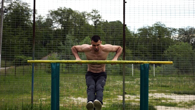 Hardy shirtless sportsman doing exercises on parallel bar at nature. Strong and muscular man working out at sports ground. Young athletic guy exercising outdoor. Concept of active healthy lifestyle photo