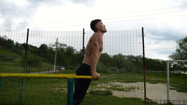 Young sportsman doing push up on parallel bars at nature. Strong sporty man exercising at sports ground. Male shirtless athlete training hard outdoor. Concept of active sportive lifestyle. Slow mo photo