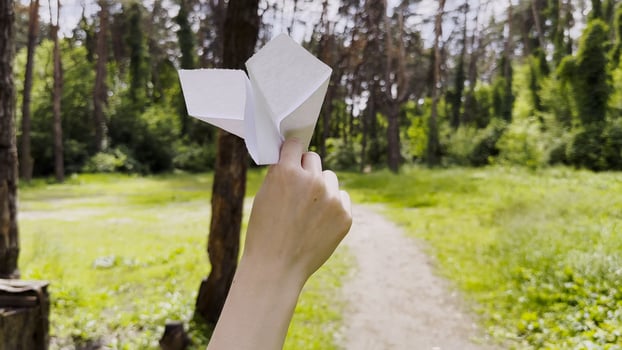 Female hand playing with paper airplane at summer forest.Girl walking with toy plane at woodland on sunny day. Young woman having fun at nature. Concept of leisure outdoor. Close up photo