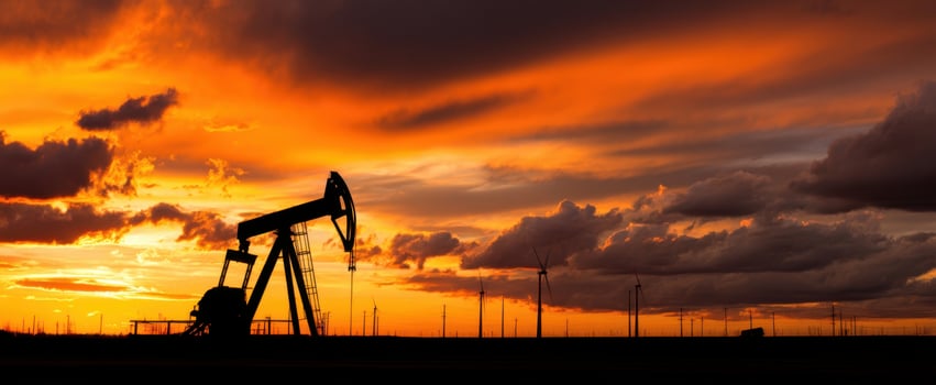 The oil pumpjack against a vibrant sunset with wind turbines in the distance. photo