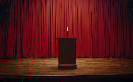 A wooden podium with a microphone stands alone before bright red curtains photo