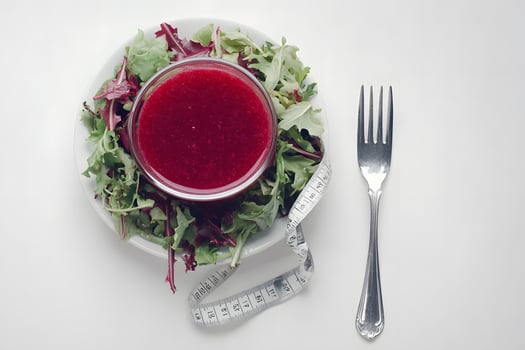 Cranberry sauce sits over salad alongside a measuring tape and fork placed on white photo