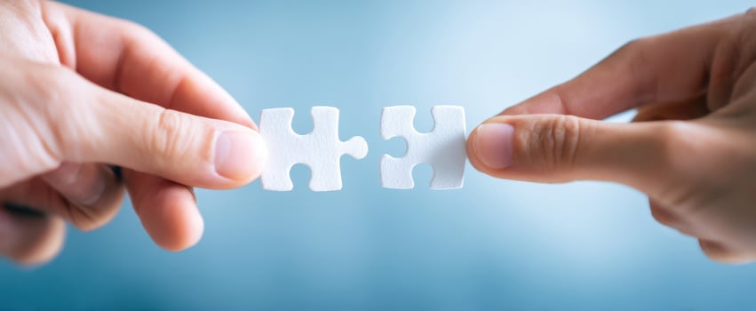 The hands connecting two white puzzle pieces against a soft blue background. photo