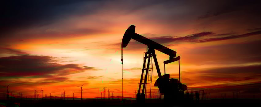 The oil pumpjack silhouetted against a vibrant sunset with wind turbines. photo