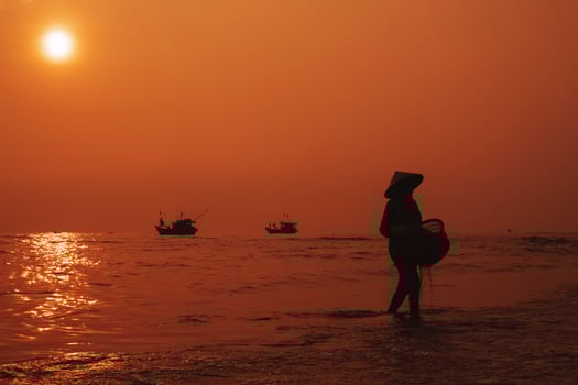 Silhouette of Vietnamese woman in straw hat on the shore of sea with ships in a fishing village in morning at sunrise in Vietnam photo